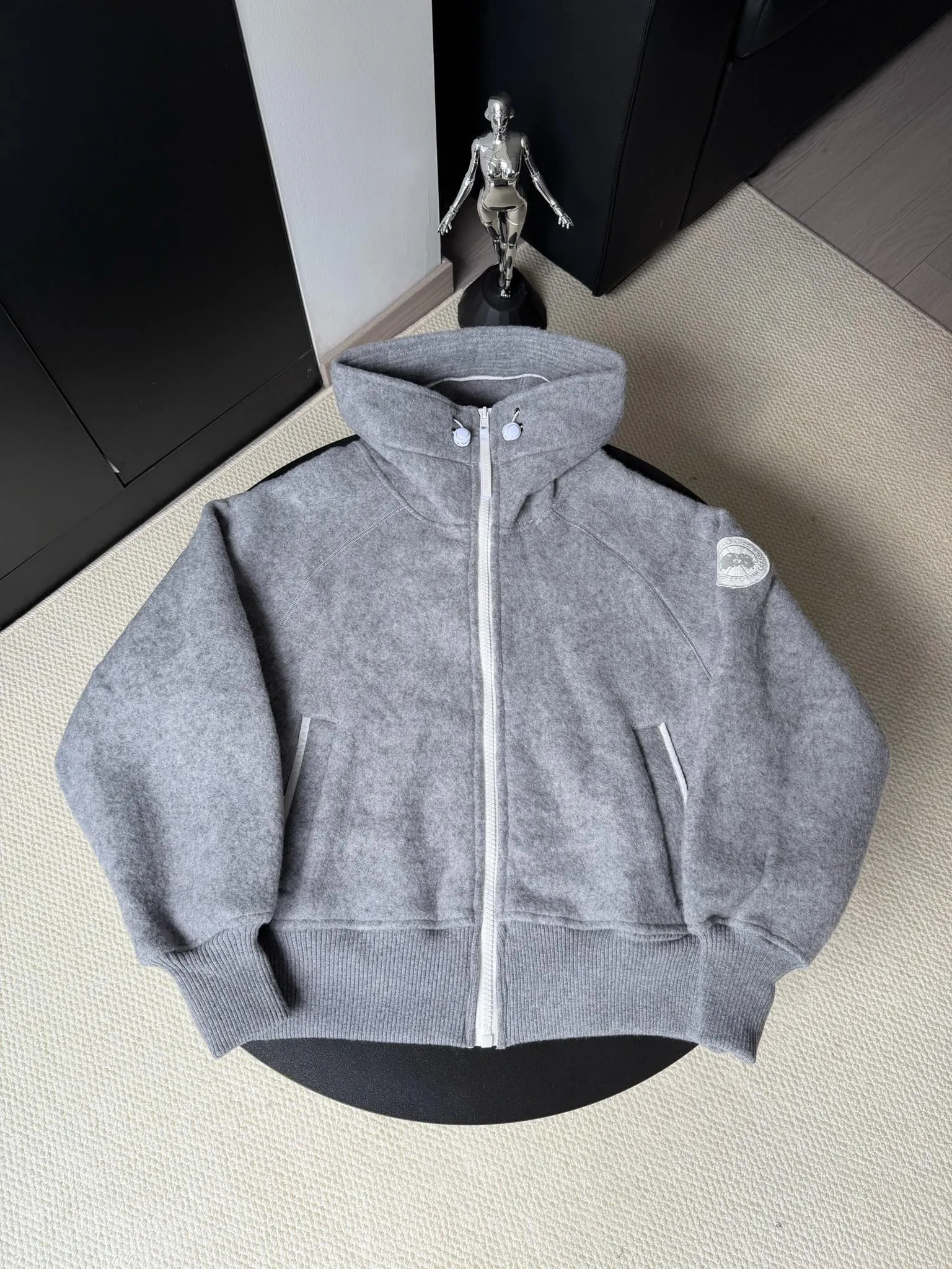 P660 Canada Goose Fleece Wool Badge Hooded Jacket Fabric selection: Wool fleece fabric blended with wool as the main body and a very small amount of spandex and polyester fiber. Wool is a core natural ingredient that provides unparalleled temperature regulation, antibacterial and anti-odor properties and a skin-friendly feel. The feeding of a small amount of spandex gives the fabric a certain degree of four-way elasticity, making it non-restrictive during daily activities. As the basis of fleece's structure, polyester fiber enhances the fabric's durability, wrinkle resistance and quick-drying properties. It contributes to the loft of the fleece and provides functions such as trapping air.  Detail 1: The sleeves and hem are closed with 2×2 ribbing. Its strong elasticity can closely fit wrists and waists of different thicknesses, forming an effective 'seal' to prevent cold wind from blowing back. It can still maintain its original shape after repeated stretching and use, and is not easy to loose and deform. And the ribbed cuffs can convey a sense of design and enhance the visual beauty.  Detail 2: The combination of hood design and elastic buckle improves warmth and windproof performance when wearing. Accessories: Customized elastic drawstring, elastic buckle, custom zipper pendant, custom armband Size: S M L Color: black gray coffee rice pink